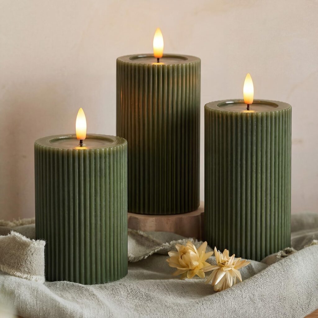Three ribbed forest green pillar candles on a wooden tray with a small white flower.