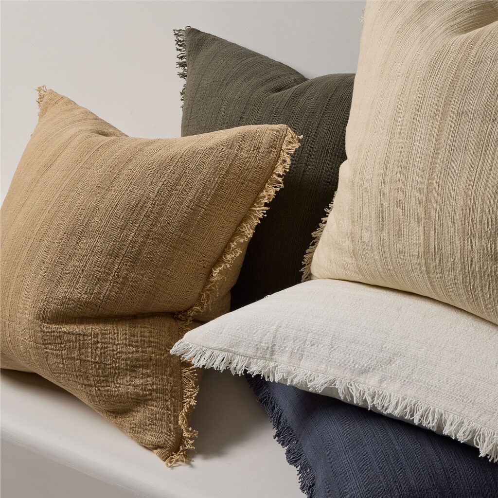 Close-up of layered neutral and tan linen throw pillows on a cream sofa.