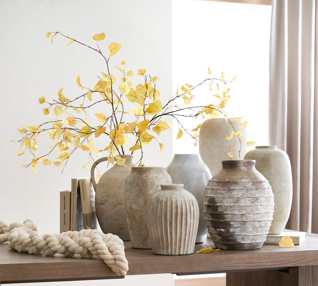 Close-up of modern beige ceramic vases with dried natural florals on a light wood shelf.