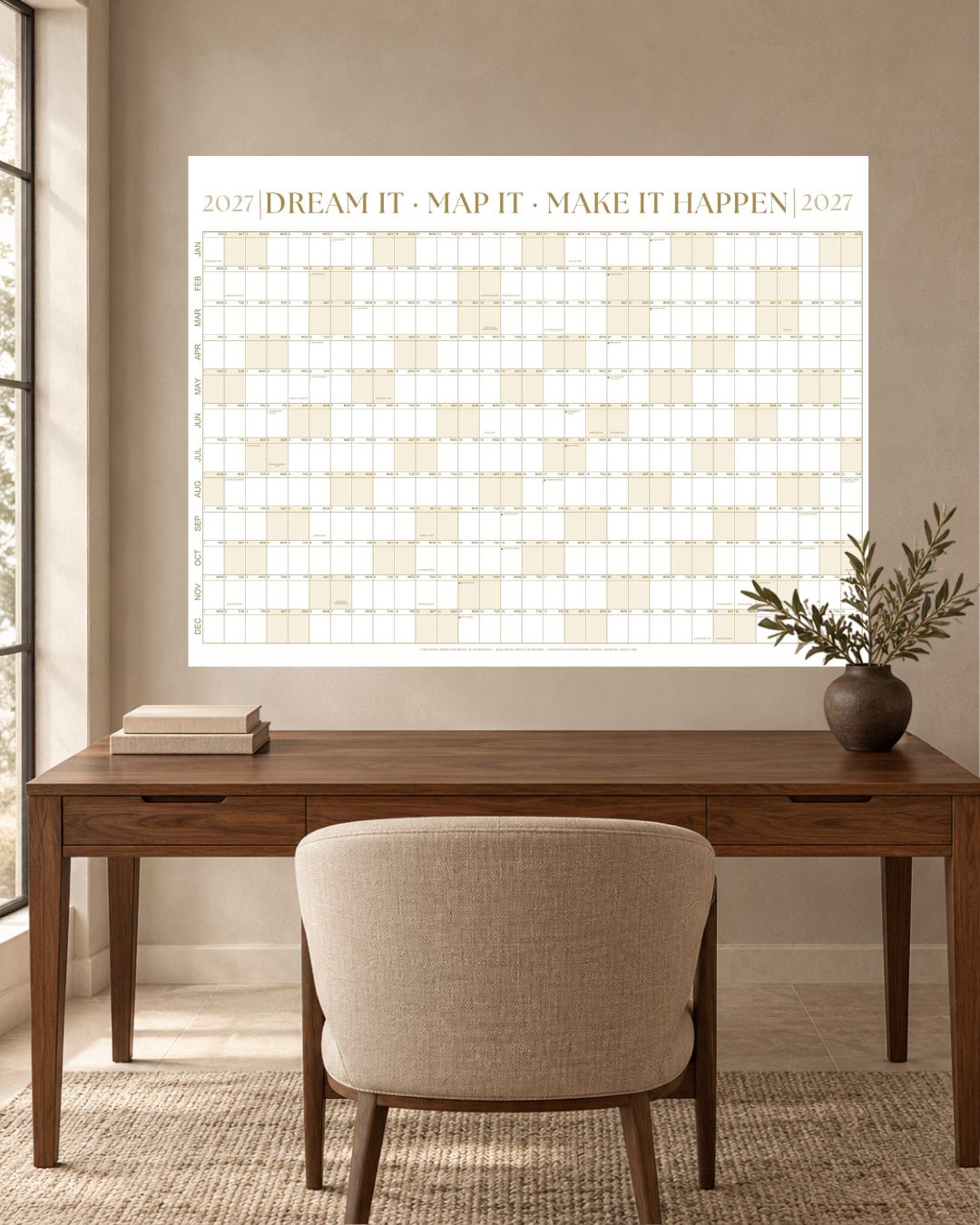 Sandstone Gold 2027 wall calendar hanging above a walnut desk with an upholstered chair and a vase of olive branches